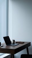 Minimalist workspace with open laptop, coffee cup, and notebook on wooden desk near bright window, suitable for business and productivity concepts.