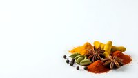 Colorful spices and herbs collection with star anise, turmeric, paprika, cardamom pods and peppercorns arranged on white background for cooking.