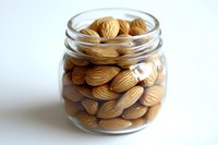 Roasted almonds in glass jar isolated on white background, ready for food packaging, healthy snack storage, and nutritional content design projects.
