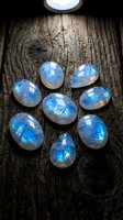 Blue moonstone gemstones arranged in circle on rustic wooden surface with natural lighting for jewelry making and crystal healing practices.