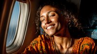 Happy young African American woman smiling while traveling in airplane cabin, enjoying flight journey with warm sunlight through window.