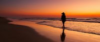 Silhouetted runner jogging along sandy beach at golden sunset, athletic person exercising by ocean waves during dawn or dusk for fitness and wellness content.