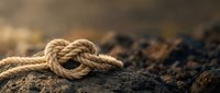 Natural jute rope with nautical knot on weathered rock surface, outdoor adventure and maritime concept for rustic design projects.