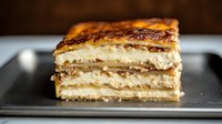 Layered vanilla cream pastry slice with caramelized sugar top on dark plate. Close up view shows flaky puff pastry layers filled with custard cream.