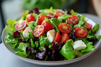 Fresh mixed green salad with cherry tomatoes, mozzarella pearls and purple lettuce leaves on white plate. Close up view of healthy Mediterranean dish.