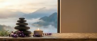 Zen spa composition with balanced stone stack, burning candle and lavender on wooden surface overlooking misty mountain landscape for wellness relaxation.