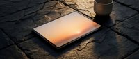 Laptop displaying warm sunset glow on dark textured surface with coffee cup, suitable for technology, business, and creative workspace concepts.