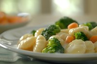 Creamy pasta with fresh broccoli florets and diced carrots on white plate, ideal for food blogs, recipes, and healthy eating content.