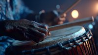 Close-up of hands playing traditional djembe drum with warm stage lighting creating atmospheric music performance scene for cultural events.