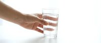 Person with medium skin tone holding a clear glass of water against a white background, suitable for health, wellness, hydration, and lifestyle design projects.