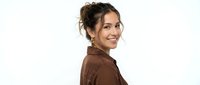Young Hispanic woman with curly hair in messy bun wearing brown shirt smiling at camera on white background isolated for design use.