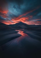Dramatic sunset illuminates winding river through dark mountain landscape, with fiery orange clouds reflecting in water against deep blue twilight sky.
