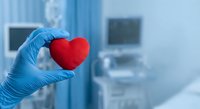 Medical professional in blue gloves holding red heart symbol in hospital setting representing cardiology care, healthcare compassion and cardiac treatment services.
