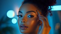 Young African American woman with glowing skin in neon blue lighting, dramatic makeup and glossy lips against blurred bokeh background, modern beauty portrait.
