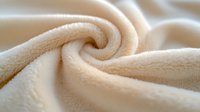 Soft cream colored fleece fabric swirled in spiral pattern showing plush texture and cozy material detail, suitable for backgrounds and textile design projects.