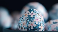 Decorative Easter egg covered in delicate blue and white flower pattern with pink accents, creating elegant spring holiday decor against dark background.