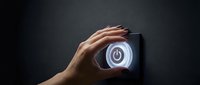 Close-up of hand pressing illuminated power button on dark wall, symbolizing energy control, technology activation, and smart home automation systems.