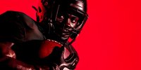 Dramatic silhouette of American football player in protective gear against vibrant red background, showcasing strength and determination in sports.