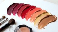 Colorful makeup palette swatches displaying warm tones from burgundy to coral with professional brushes and compact powder for beauty tutorials.