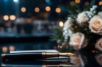 Elegant fountain pen on reflective surface with soft bokeh lights and delicate pink roses in background, creating luxurious atmosphere for business and celebration themes.