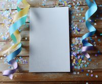 Blank white paper mockup with colorful curled ribbons and confetti scattered on rustic wooden background. Festive celebration layout for party invitations.