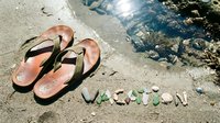 Flip flops and colorful stones spelling vacation on wet sandy beach shore, summer holiday travel concept.