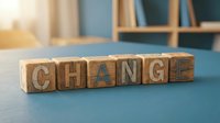 Wooden letter blocks spelling CHANGE on blue surface with bookshelf background. Business transformation and personal development concept for motivation content.