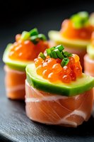 Delicate salmon rolls topped with fresh cucumber, red caviar and chives served on black slate. Elegant Japanese fusion appetizer with vibrant colors and textures.