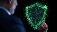 Businessman pointing at glowing green shield made of particles and light effects, representing digital security and cyber protection on dark background.