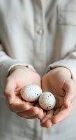 Close-up of hands holding two speckled eggs, wearing neutral linen shirt. Suitable for Easter, spring, agriculture, farming, and food-related designs.