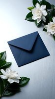 Navy blue envelope surrounded by white gardenia flowers on elegant gray surface for wedding invitations and special occasions.
