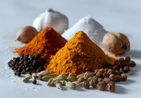 Colorful spice piles including turmeric, paprika, and black pepper with whole spices like garlic, nutmeg, and cardamom on white surface for cooking and seasoning.
