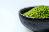 Fresh matcha green tea powder in black ceramic bowl on white background, selective focus with copy space for wellness and healthy lifestyle designs.