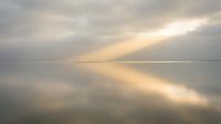 Serene lake at dawn with golden sunlight breaking through soft clouds, creating peaceful reflections on calm water surface for meditation and wellness content.