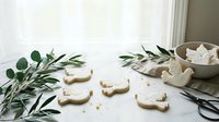 Homemade sugar cookies shaped like cute animals with powdered sugar dusting on marble surface with olive branches for holiday baking and festive treats.