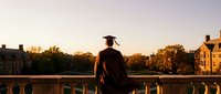 Graduate in cap and gown watching sunset over university campus, celebrating academic achievement and future opportunities ahead.