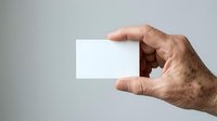 Mature male hand holding blank white business card against neutral background, ready for branding and corporate identity design projects.