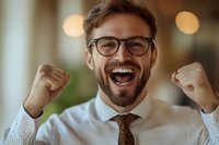 Young Caucasian businessman with glasses and beard celebrating success with raised fists and excited expression. Professional portrait showing joy and achievement.