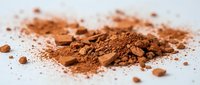 Pile of cocoa powder and crushed cocoa nibs scattered on white surface, suitable for food photography, baking, and culinary content.