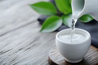 Pouring fresh water into white ceramic bowl on wooden surface with green leaves creating peaceful spa atmosphere for wellness and relaxation rituals.