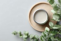 Minimalist wooden tray with ceramic bowl of milk or cream surrounded by fresh eucalyptus branches on light background, perfect for spa or wellness design.