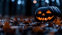 Glowing carved black pumpkin with classic jack o'lantern face sits among fallen autumn leaves at dusk, creating spooky Halloween atmosphere with blurred bokeh lights in background.