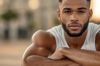 Young African American male model with well-groomed beard wearing white tank top, looking confidently at camera. Natural outdoor lighting creates warm atmosphere.