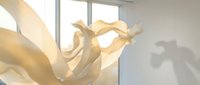 Abstract golden flowing ribbons creating dynamic sculptural forms in bright modern interior space with natural lighting and soft shadows.
