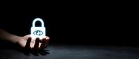 Hand holding glowing padlock with eye symbol representing digital security, privacy protection, and data encryption for cybersecurity concepts.