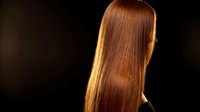 Young woman with long straight auburn hair in dramatic golden lighting against dark background for beauty and hair care concepts.