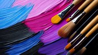 Vibrant pink, blue, and black paint strokes with professional wooden makeup brushes arranged diagonally on dark background, showcasing artistic cosmetic application.