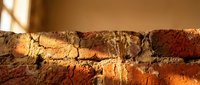 Weathered brick wall with cracked mortar and warm sunlight casting shadows, showing aged construction materials and rustic architectural texture.