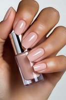 Elegant nude pink manicure on medium skin tone female hand holding nail polish bottle, showcasing glossy gel nails in natural lighting for beauty and cosmetics.