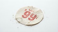 Vintage paper circle with red number 99 on textured white background. Aged distressed label with torn edges and weathered appearance for retro design projects.